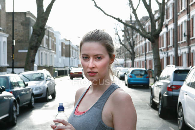Portrait of young female runner in street drinking water — Stock Photo