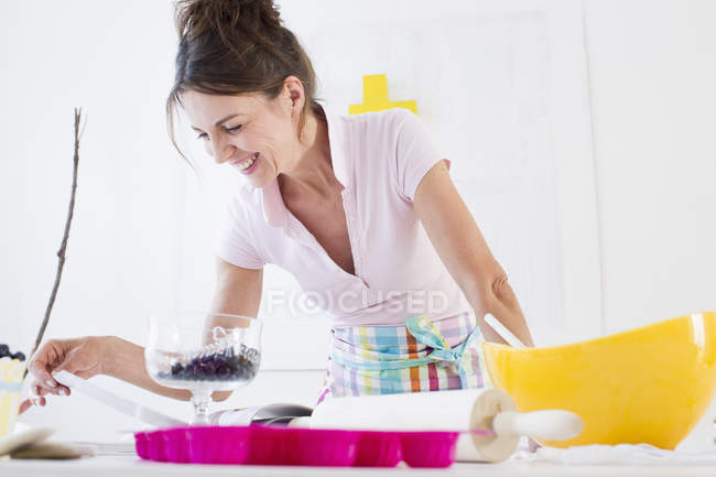 Зріла жінка в фартусі готує їжу, дивлячись вниз посміхаючись — стокове фото