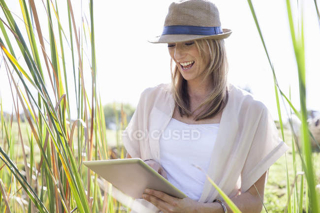 Mulher adulta média sentada em grama longa, usando comprimido digital — Fotografia de Stock