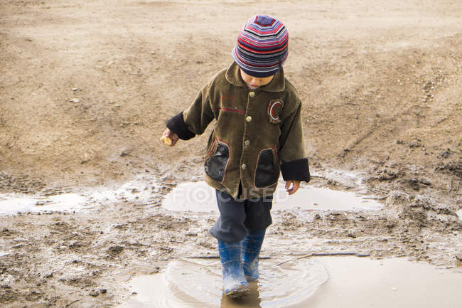 Male toddler wearing rubber boots paddling in puddle — Stock Photo