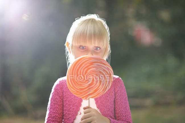 Portrait of girl with lollipop in front of her face in garden — Stock Photo