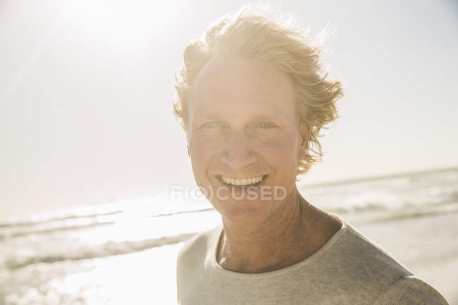 Retrato del hombre por el océano mirando a la cámara sonriendo - foto de stock