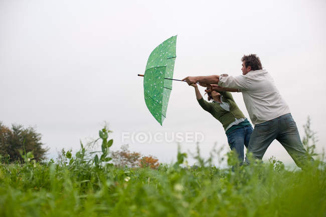 Couple with umbrella in windy field — Stock Photo