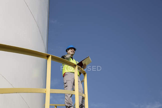 Male worker standing on steps of storage container at fuel depot, low angle view — Stock Photo