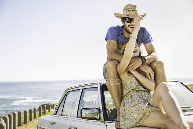 Casal adulto médio sentado no topo do carro na estrada da costa, Cidade do Cabo, África do Sul — Fotografia de Stock