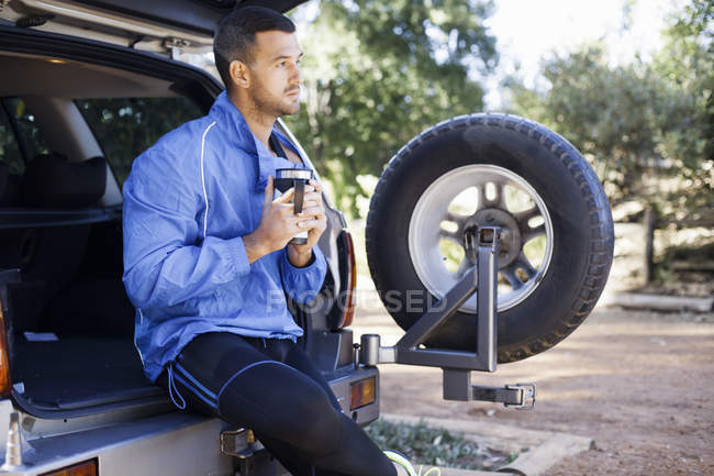 Male jogger holding flask at back of car — Stock Photo