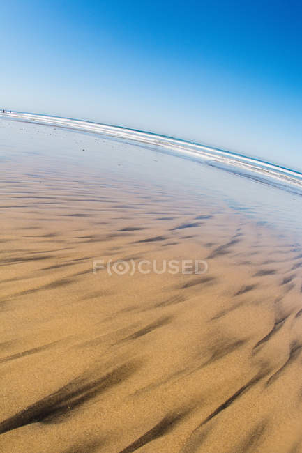 Arena con olas oceánicas en la distancia - foto de stock