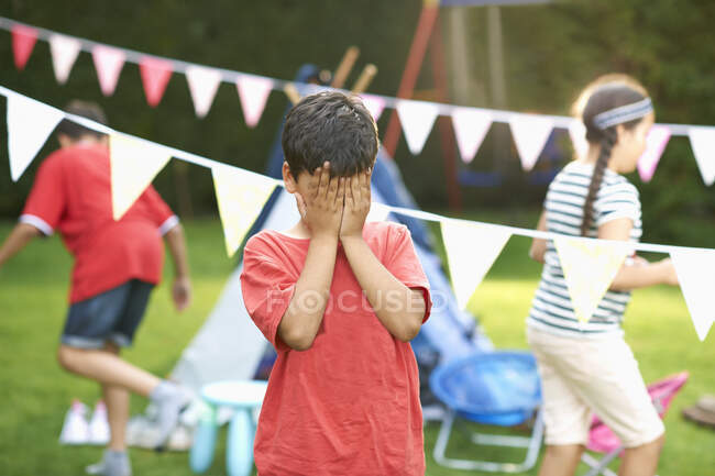 Junge verdeckt seine Augen nach Verstecken mit Bruder und Schwester im Garten — Stockfoto