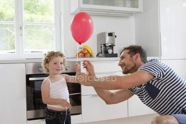 Chica sosteniendo globo con el padre en la cocina - foto de stock