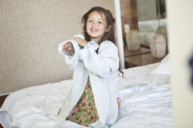 Portrait of young girl sitting on bed wearing oversized white shirt — Stock Photo