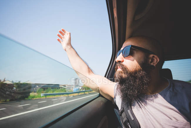Бородатый мужчина высовывает руку из окна машины на шоссе, Гарда, Италия — стоковое фото
