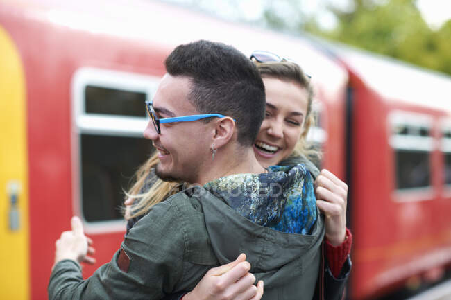 Хетеросексуальна пара обіймається на залізничній станції, посміхаючись — стокове фото