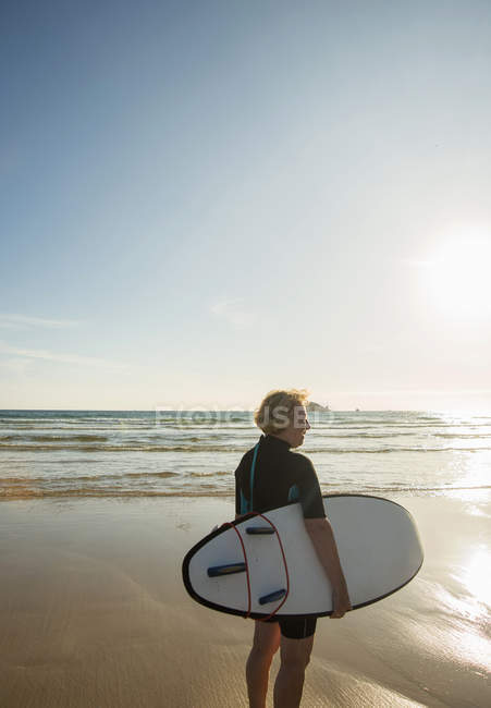 Senior female surfer standing on beach with surfboard, Camaret-sur-mer, Bretaña, Francia - foto de stock