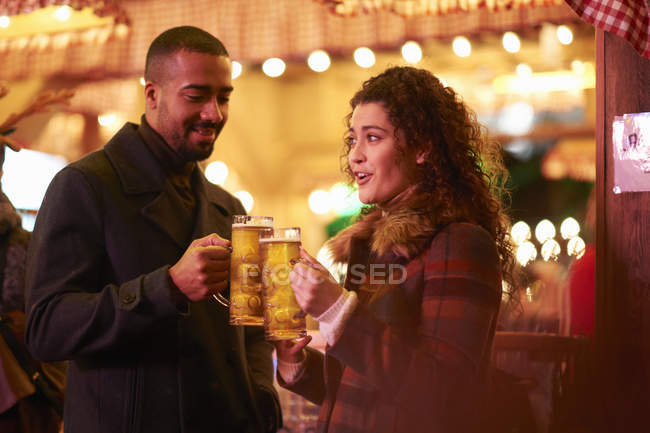 Casal na noite fora segurando vidro na cerveja fazendo um brinde — Fotografia de Stock