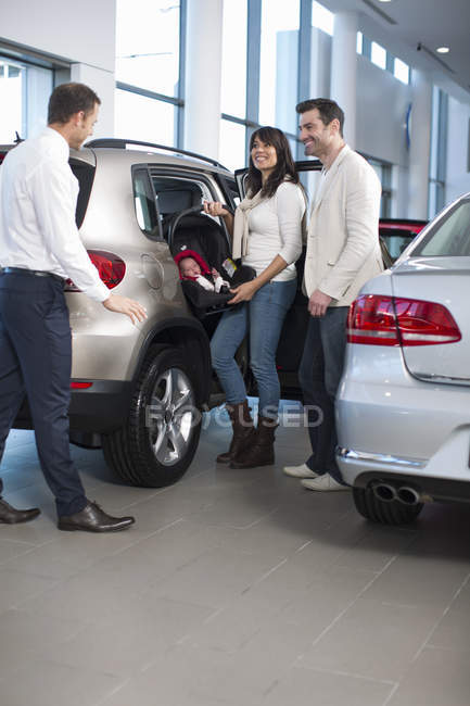 Salesman chatting to family with baby girl in car dealership — Stock Photo