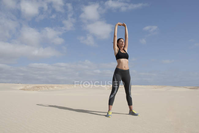 Mitte erwachsene Frau übt mit erhobenen Armen am Strand — Stockfoto