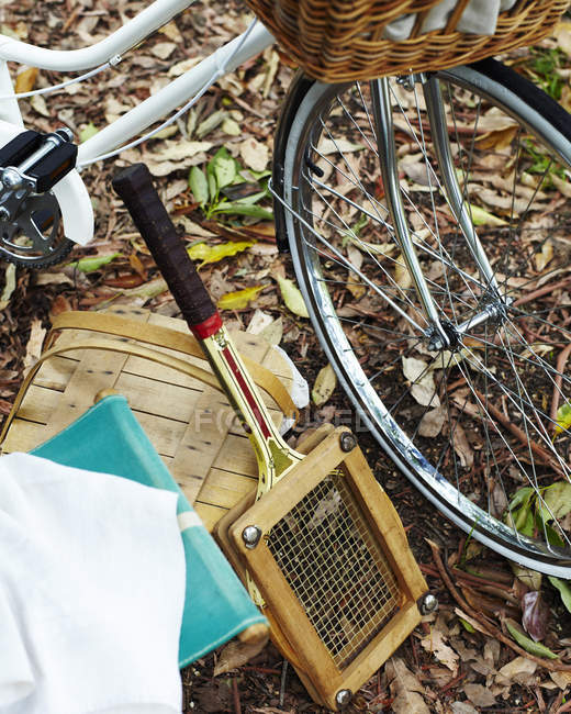 Bicicletta, cestino da picnic e racchetta da tennis in autunno lasciare il terreno coperto — Foto stock