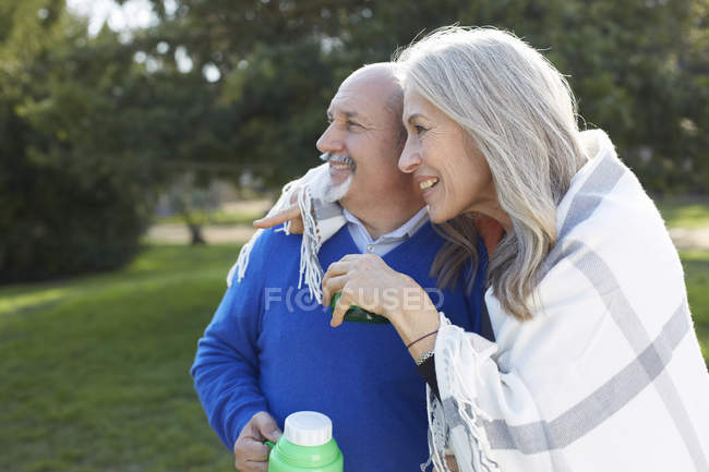 Paar in Decke gehüllt hält Getränkeflasche und schaut lächelnd weg — Stockfoto