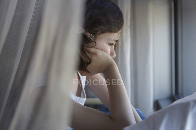 Sullen girl reclining on bed resting on elbow — Stock Photo