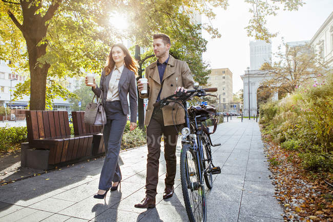Casual businessman and woman pushing bike through park — Stock Photo
