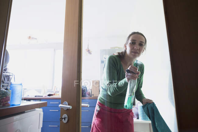 Vista através da porta de vidro da mulher adulta média esguichando produto de limpeza — Fotografia de Stock