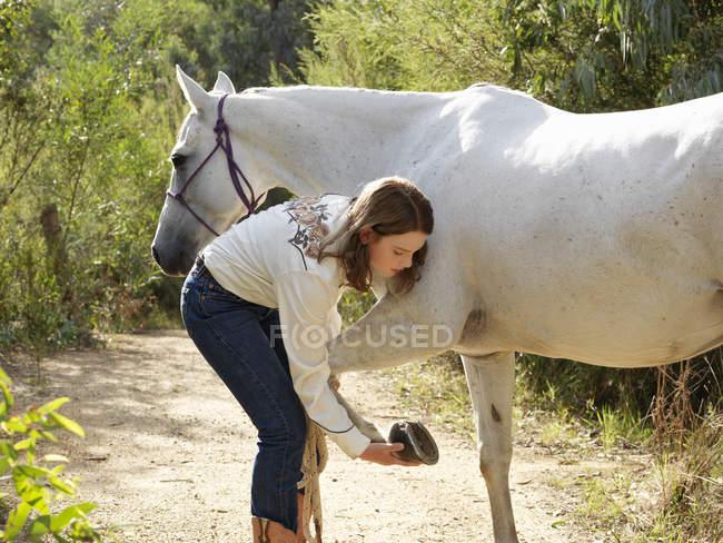 Adolescente chequeando pezuñas de caballo - foto de stock