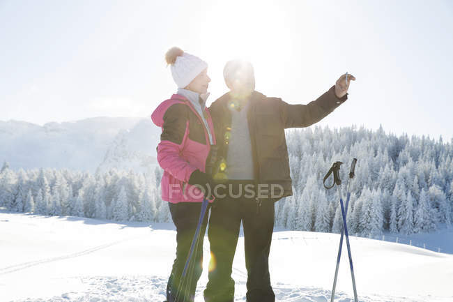 Coppia senior su paesaggi innevati con smartphone per scattare foto, Sattelbergalm, Tirolo, Austria — Foto stock