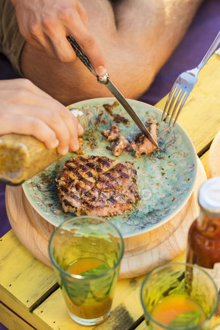 Cropped image of  two people cutting meat and pouring condiment onto plate — Stock Photo