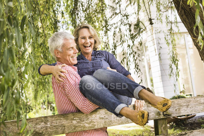Husband carrying wife onto garden fence — Stock Photo