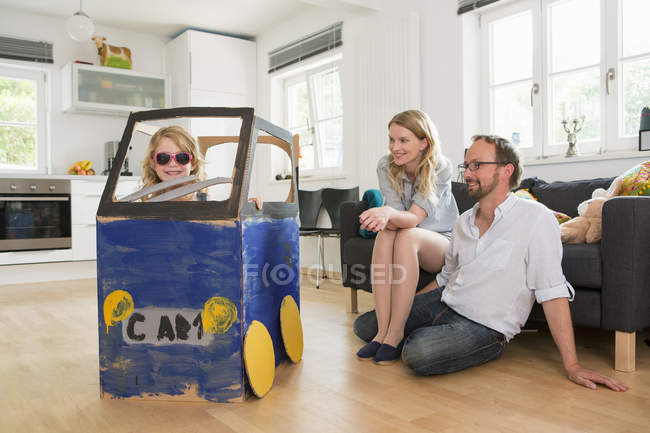 Eltern beobachten Tochter in selbstgebautem Spielzeugauto — Stockfoto