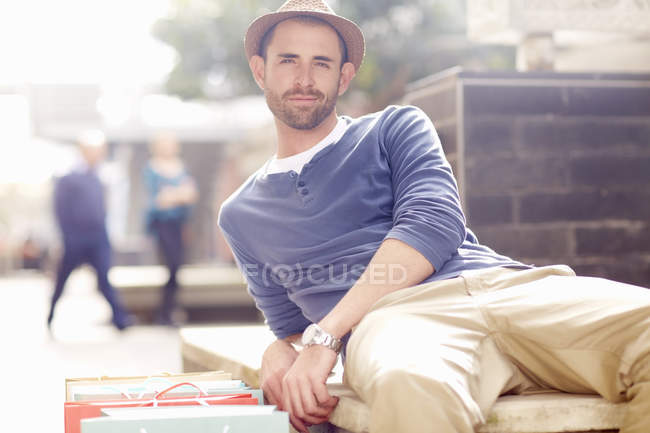 Mittlerer erwachsener Mann entspannt auf Sitz, Einkaufstüten neben sich — Stockfoto