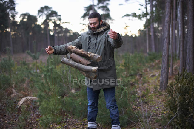Молодой человек сбрасывает дрова для костра в лесу — стоковое фото