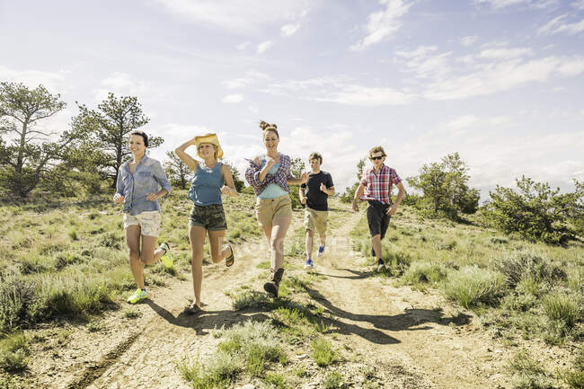 Adolescente y amigos adultos corriendo en pista de tierra, Bridger, Montana, EE.UU. - foto de stock