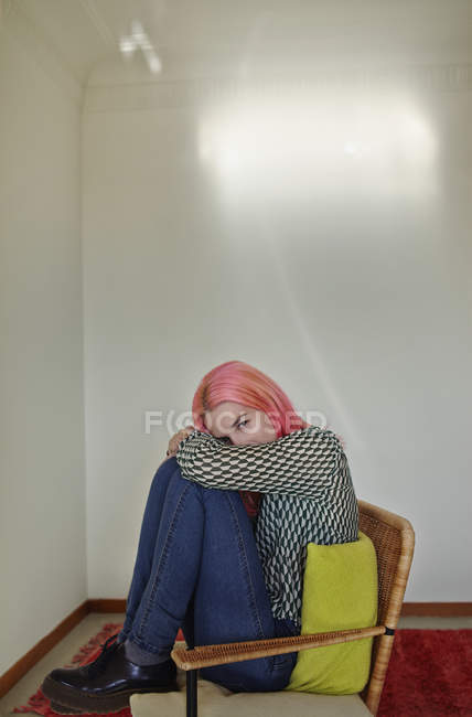 Seitenansicht einer Frau mit rosafarbenen Haaren, die im Stuhl sitzt und auf Knien in die Kamera blickt — Stockfoto