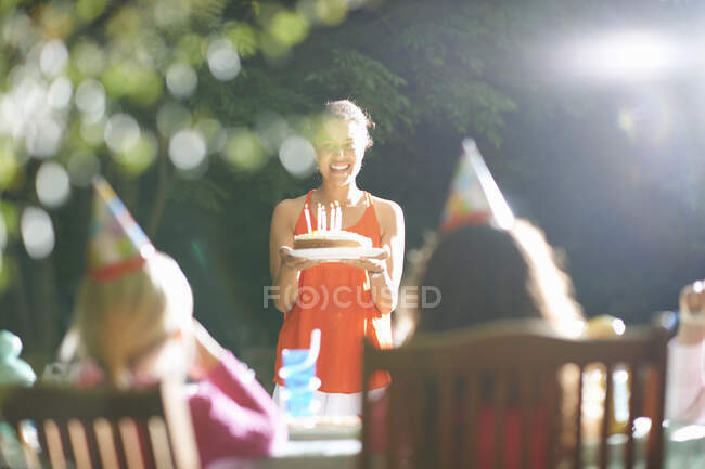 Madre llevando pastel de cumpleaños a la mesa en el jardín fiesta de cumpleaños - foto de stock