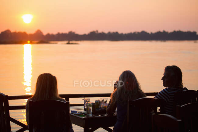 Vue arrière de trois amis adultes regardant le coucher du soleil sur le Mékong, Don Det, Laos — Photo de stock