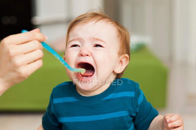Chorando bebê sentado na cadeira sendo alimentado — Fotografia de Stock