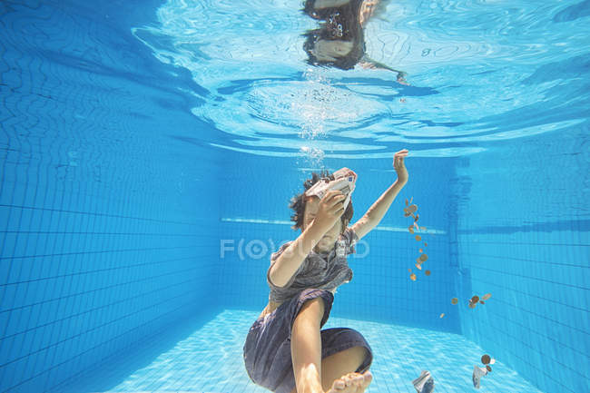 Vista submarina del niño en la piscina agarrando billetes y monedas de euro - foto de stock