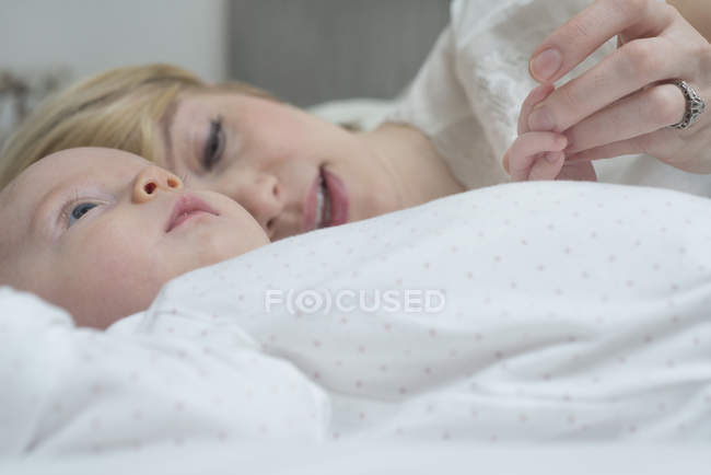 Madre acostada con la niña en la cama - foto de stock