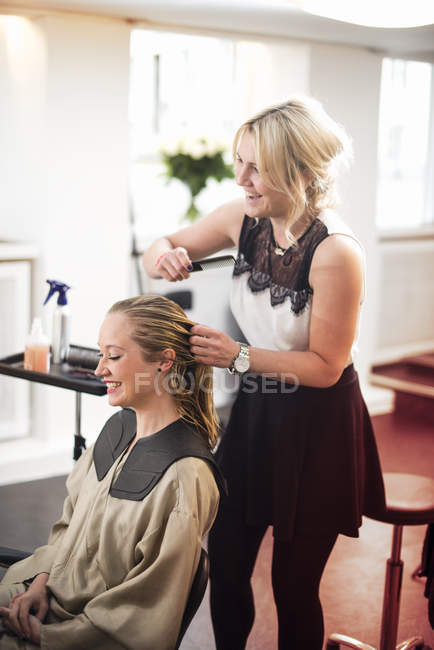 Coiffeur peigner les cheveux des clientes dans le salon — Photo de stock