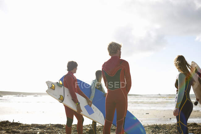 Group of surfers standing on beach, holding surfboards, rear view — Stock Photo