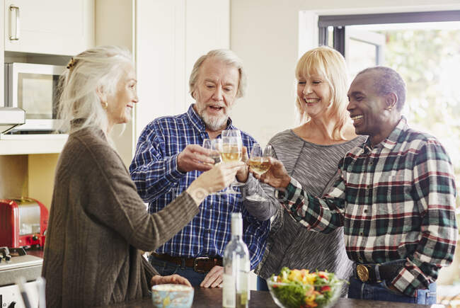 Senior friends toasting with wine in kitchen — Stock Photo