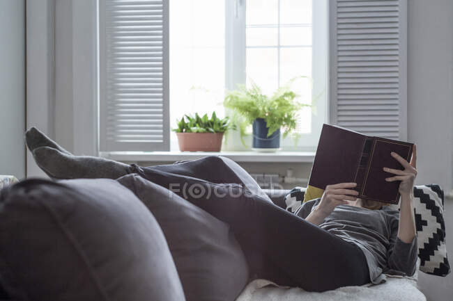 Donna sdraiata sul divano del salotto a leggere un libro — Foto stock