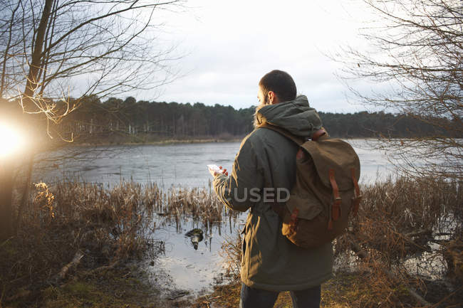 Jeune randonneur masculin au bord du lac lire la carte — Photo de stock