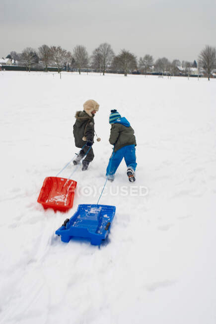 Мальчики бегают по снегу с санями — стоковое фото