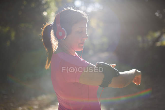 Side view of mature woman wearing headphones preparing armband — Stock Photo