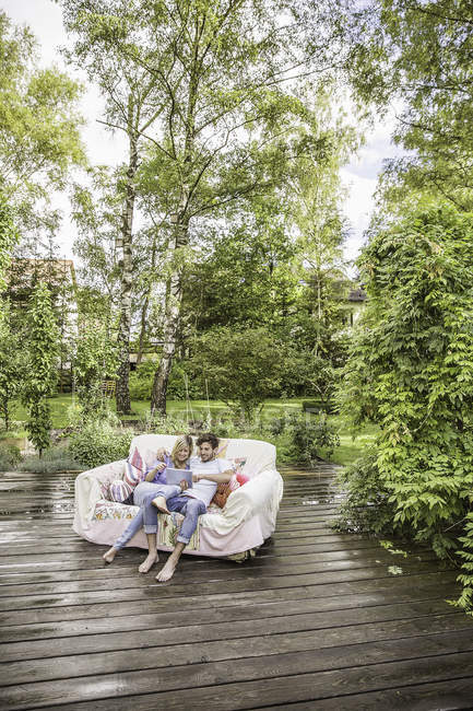 Vista de ángulo alto de la pareja sentada en un sofá vintage en el jardín y utilizando una tableta digital - foto de stock