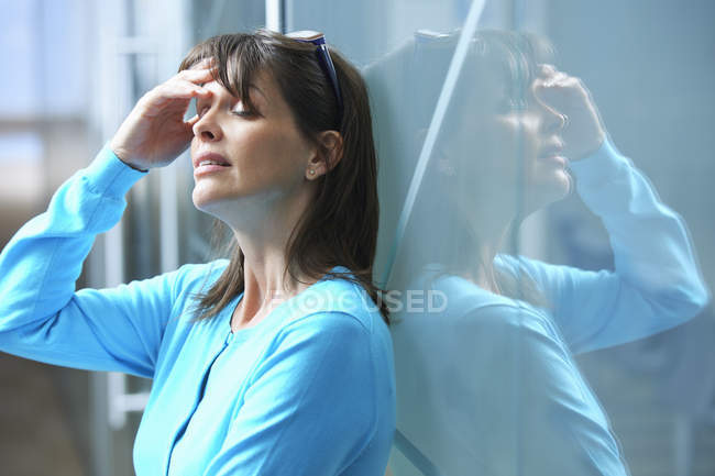 Mulher de negócios madura encostada à parede de vidro no escritório com a mão no rosto — Fotografia de Stock