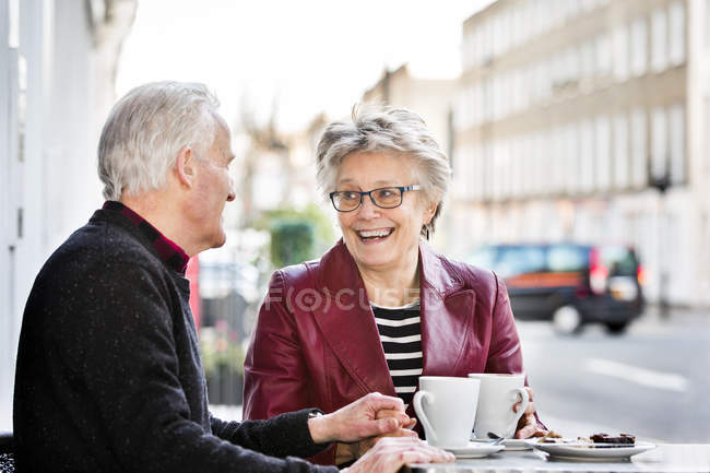 Romántica pareja de ancianos en la acera café de la mano - foto de stock