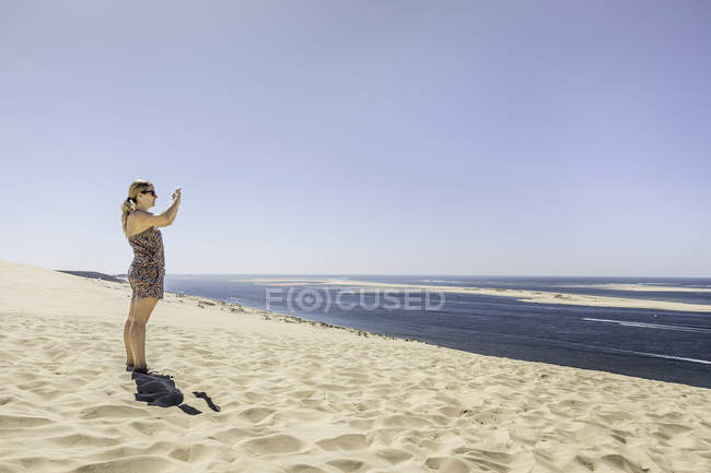 Jovem mulher fotografando mar com smartphone, Dune de Pilat, França — Fotografia de Stock